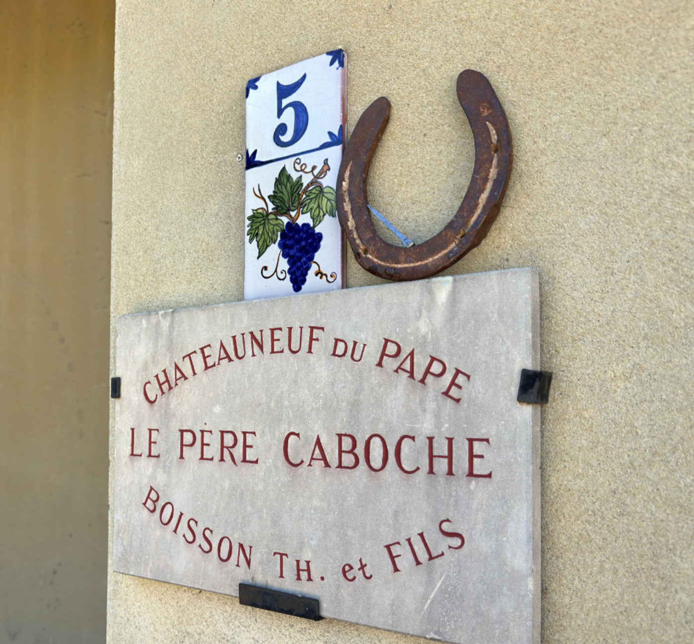 Street sign 'Le Père Caboche Boisson Th. et Fils' with horseshoe